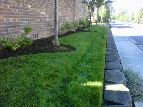 Modern Landscaping work. Perfectly cut grass on side of building with small retaining wall next to the sidewalk.