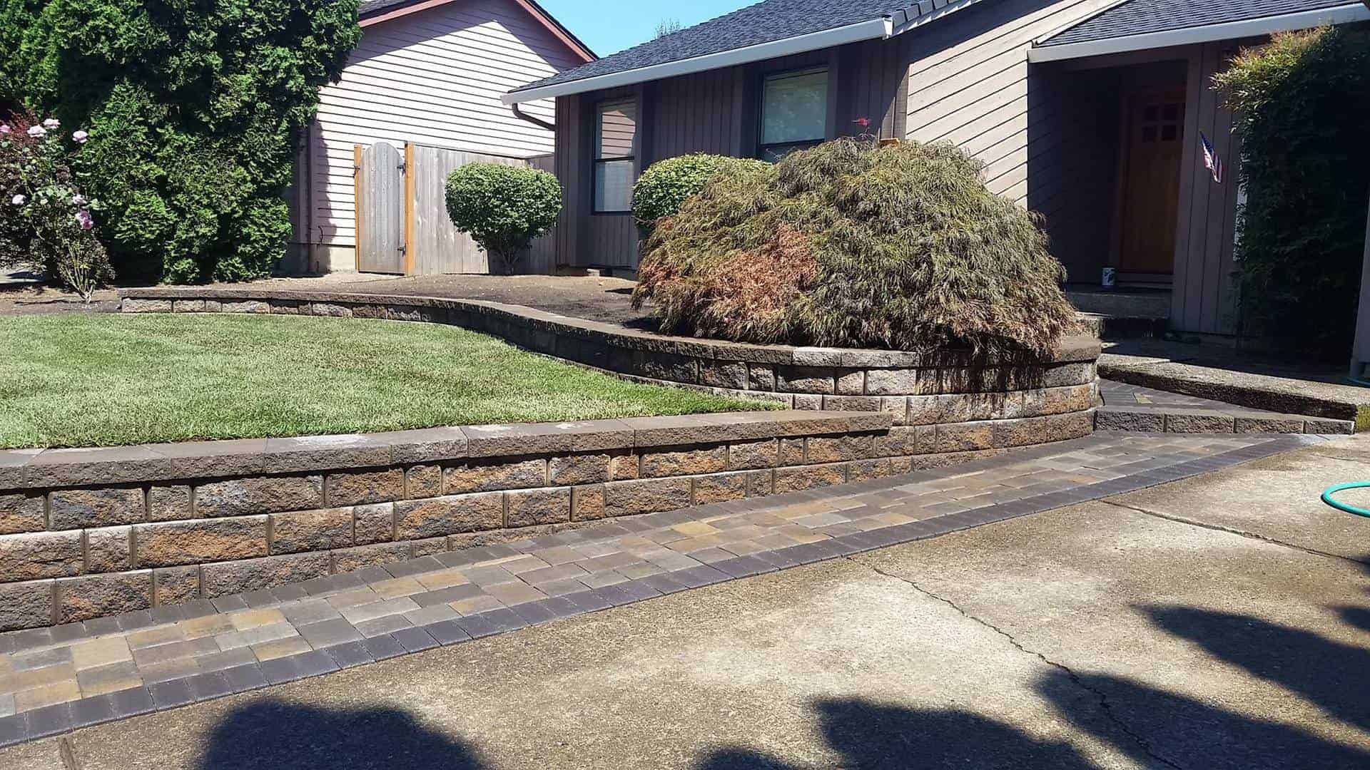 Retaining walls made out of brick pavers or natural stone with pathway and small trees trimmed and lawn maintained Pavers in POrtland
