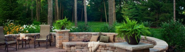 Garcias Landscaping Beaverton, Beautiful backyard with round shaped brick pavers and stone retaining wall with fire pit in the middle