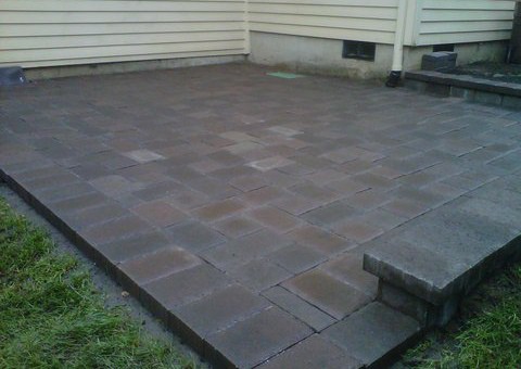 Back patio made out of grey and brown and light brick concrete pavers. Perfectly aligned forming an aesthetically pleasing square pattern.